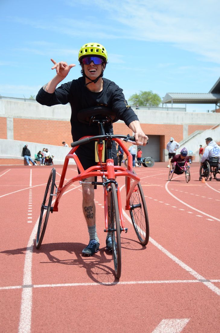 Smiling athlete in a yellow helmet gestures from a red RaceRunner on the track