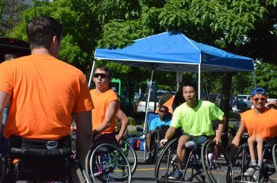 Players in orange and lime green shirts line up in wheelchairs under a canopy