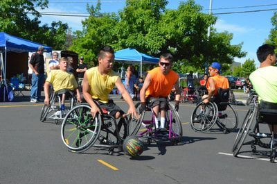 Players in yellow and orange shirts chase a loose ball across the pavement