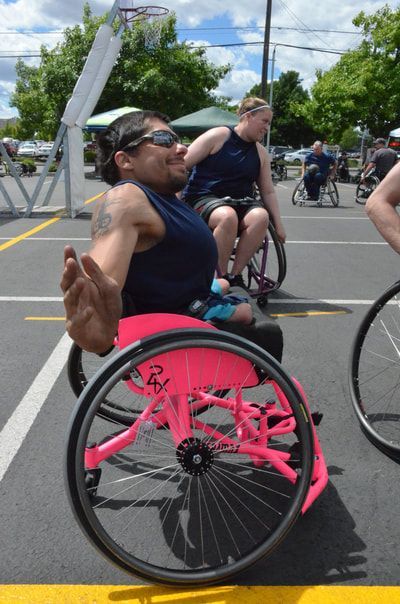 Player in a pink wheelchair spreads an arm wide and grins at the camera