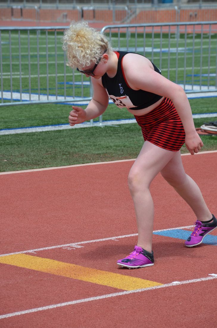 Long jumper with curly blond hair crouches on the runway before a jump