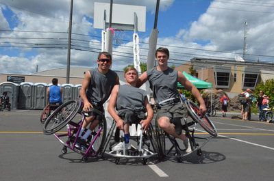 Three players in gray shirts pose under the hoop, two popping wheelies