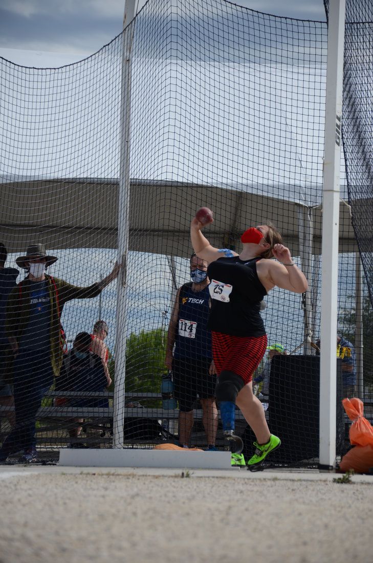 Shot putter in red and black holds the shot at the neck inside the cage