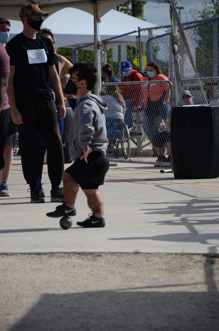 Young athlete in a gray hoodie and face mask stands by a shot on the ground