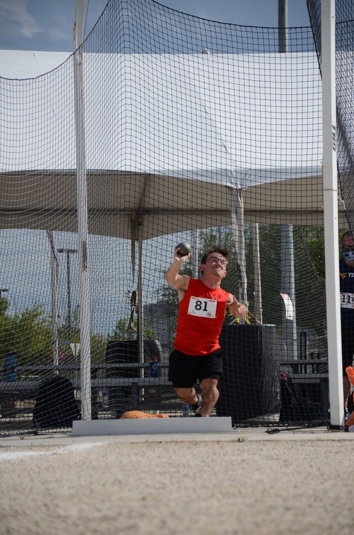 Shot putter in a red shirt, bib 81, sets up to throw inside the cage