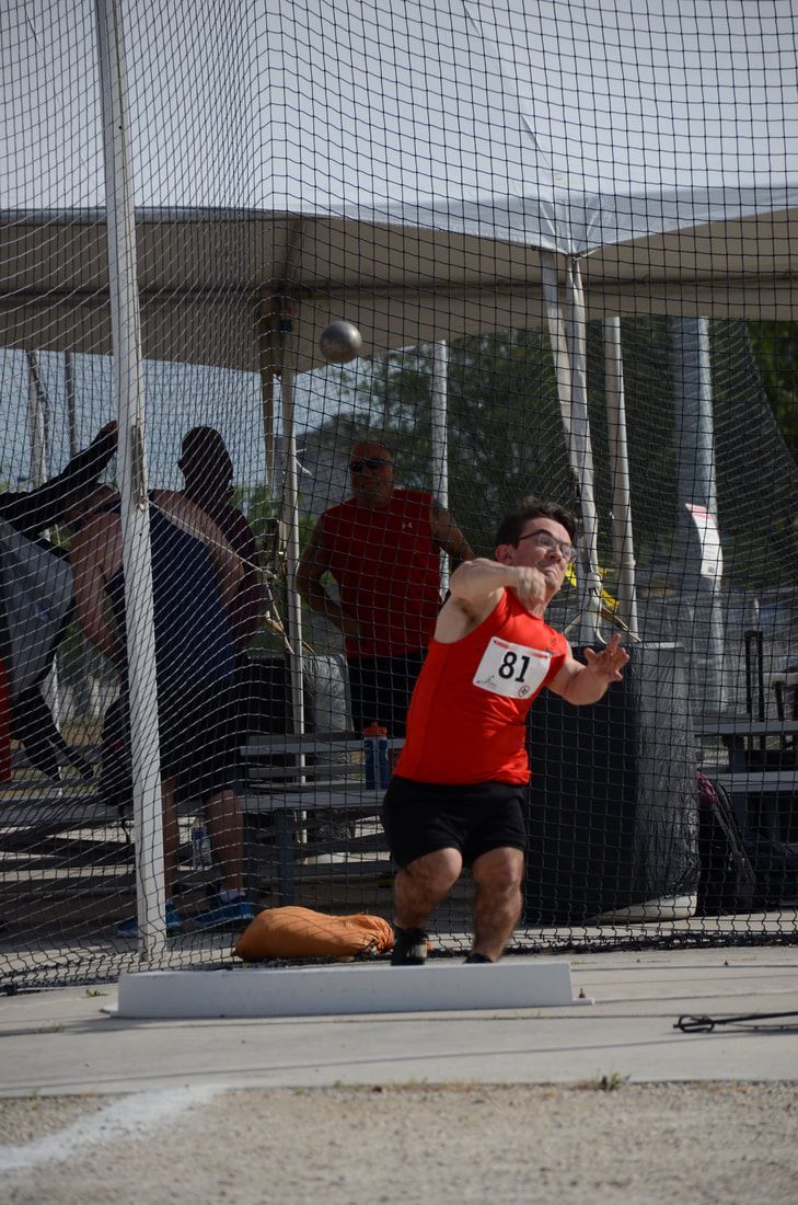 Shot putter in red, bib 81, releases the shot with the ball in midair