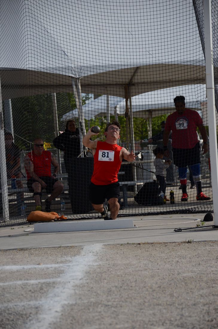 Shot putter, bib 81, crouches low to throw as people watch behind the net