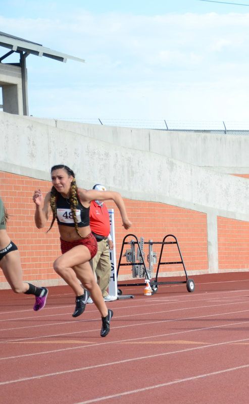 Sprinter in a black top and red shorts runs down the track at Texas Regionals