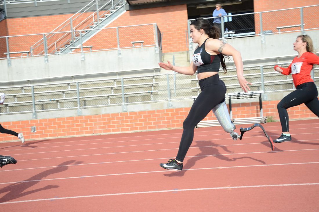 Sprinter with a running blade, bib 36, strides ahead of a runner in red