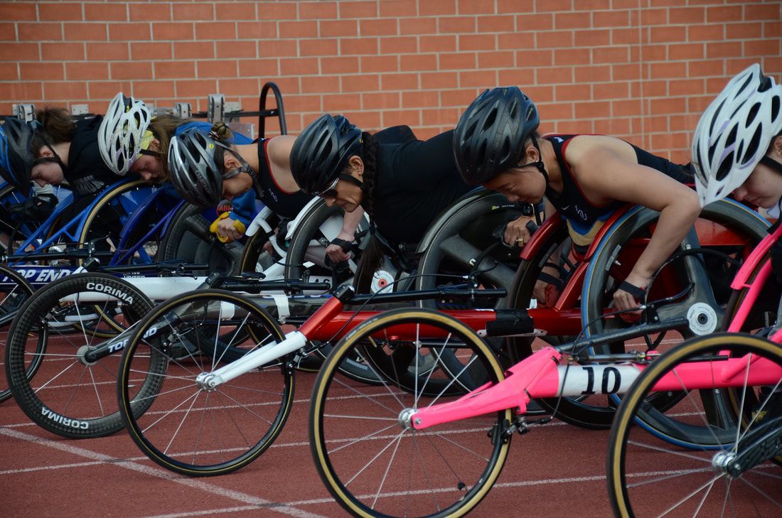 Wheelchair racers in helmets crouch in their racing chairs at the start line