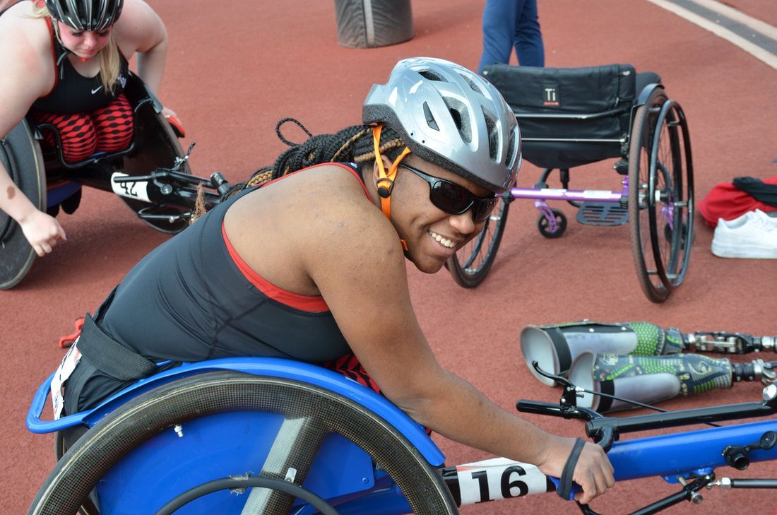 Smiling athlete in a silver helmet sits in a blue racing wheelchair