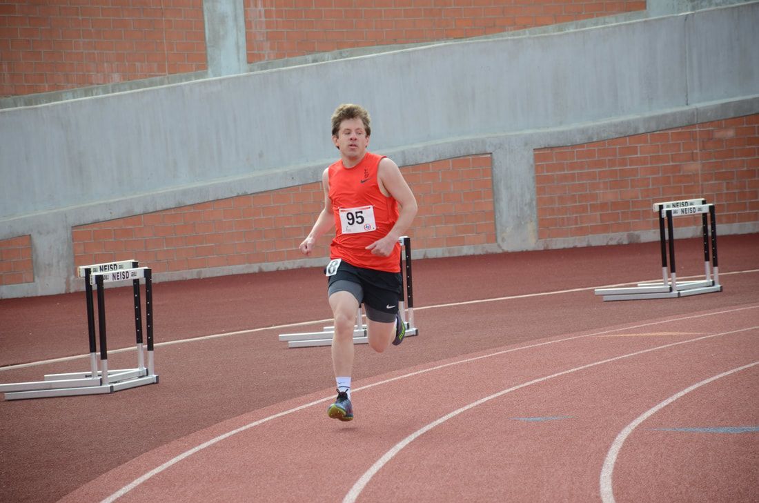 Runner in a red top, bib 95, rounds the curve past stacked hurdles
