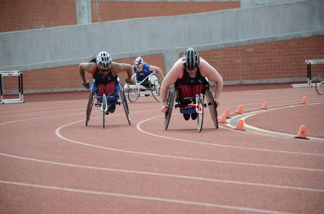 Two wheelchair racers in red and black come out of the curve side by side