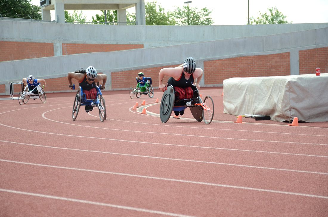 Four wheelchair racers spread out around the far curve of the track