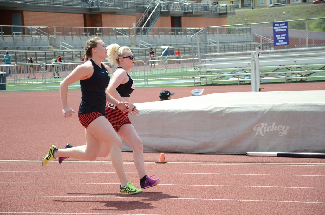 Two runners in black tops and red shorts run side by side on the track