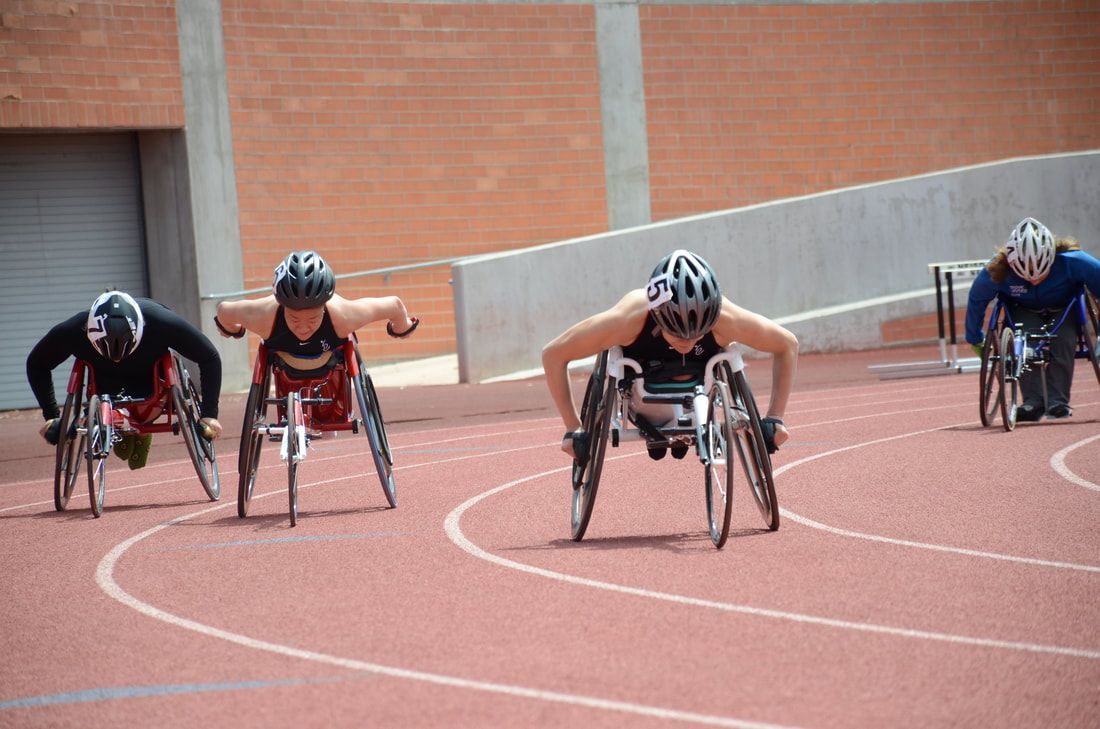 Wheelchair racers in helmets push toward the camera around the bend