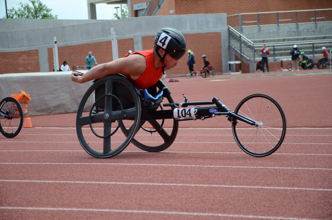 Wheelchair racer in a red top, chair 104, pushes along the straight