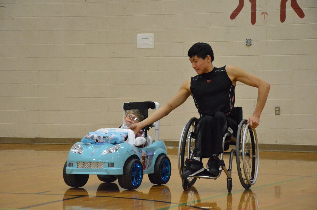Wheelchair athlete guides a child driving a light blue ride-on car