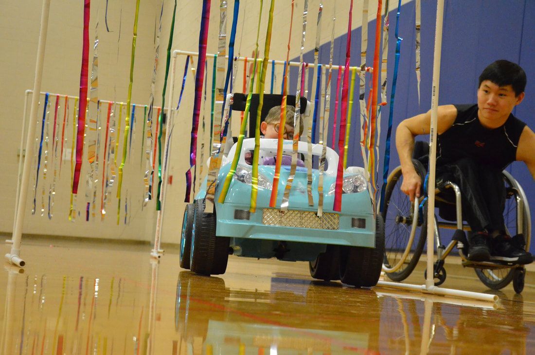 Child drives a light blue ride-on car through hanging streamers