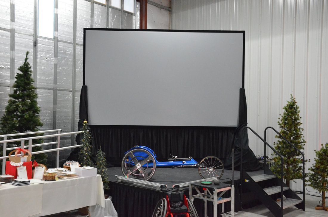 Stage with a projection screen and a blue racing wheelchair on display