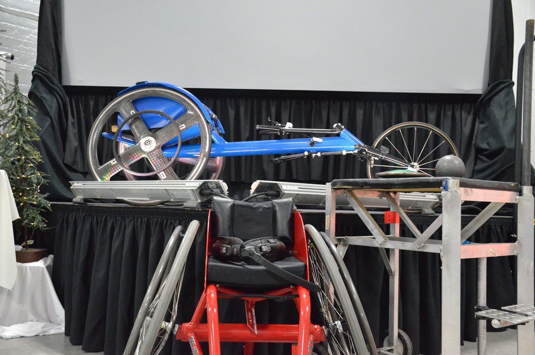 Blue racing wheelchair and red sport wheelchair displayed by the stage