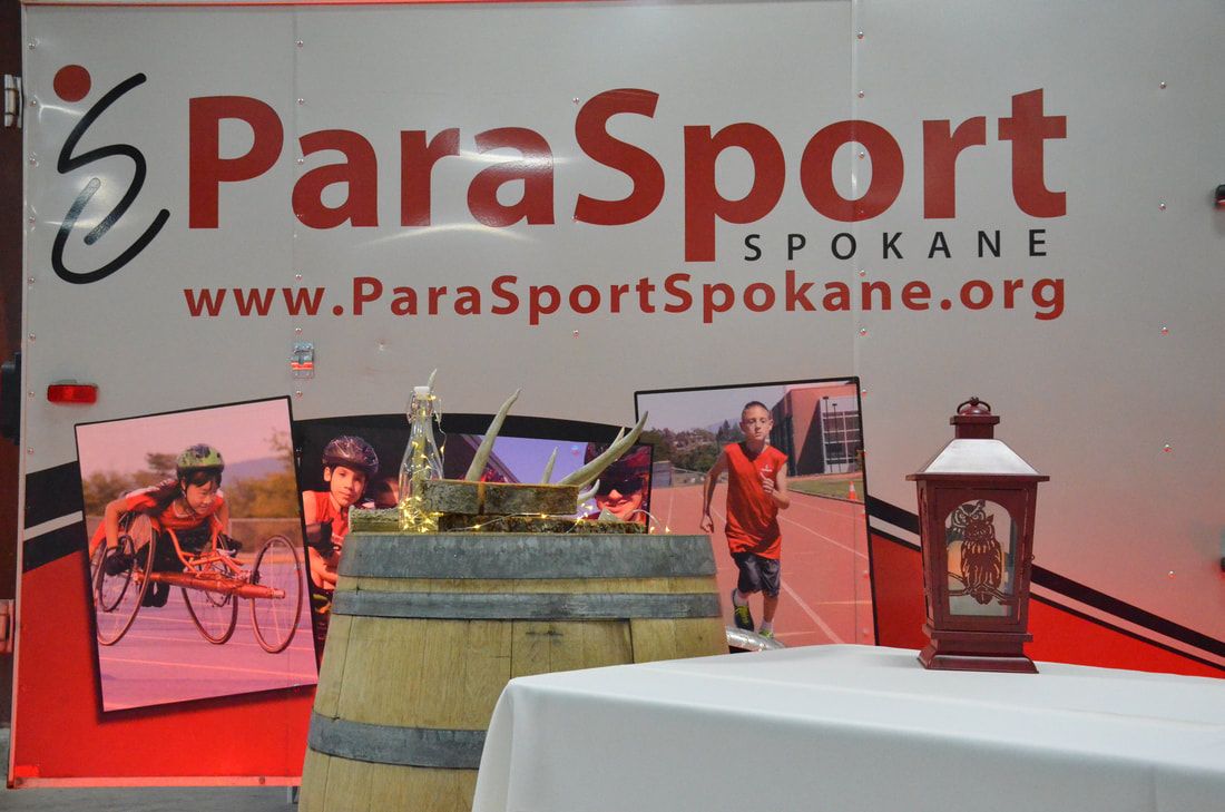 ParaSport Spokane trailer with athlete photos behind a wine barrel display