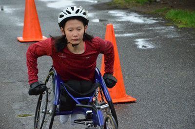 Racer in a white helmet pushes past orange cones on a rainy path