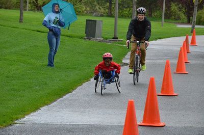 Young racer and a cyclist come down a coned path on a rainy day