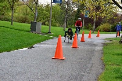 Racer and cyclist approach along a cone-lined park path