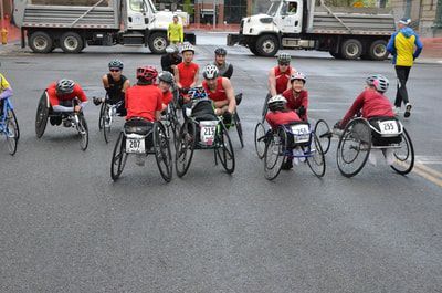 Racers with bibs gather in the street at the start of a rainy race