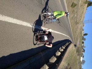 Racer in a racing wheelchair and a cyclist in green ride a highway shoulder