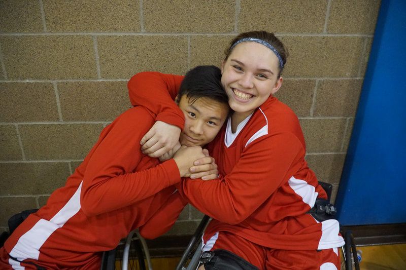 Two teammates in red warm-ups share a hug and smile