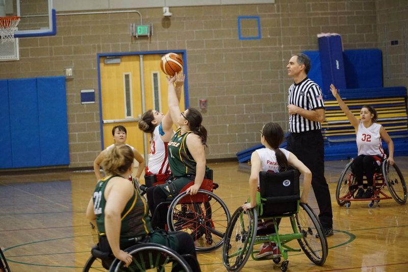 Players in white and green reach for a jump ball as the referee watches