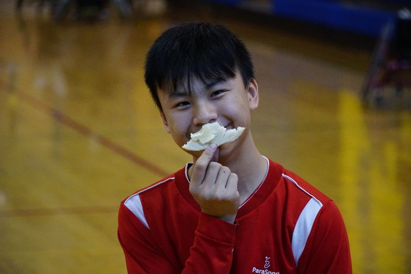 Young player in a red ParaSport warm-up grins holding a snack to his mouth