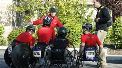 Racers in red jackets with race bibs huddle with coaches before a race