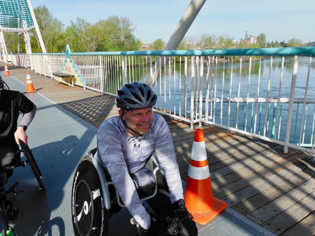 Smiling racer in a gray shirt and black helmet waits by a cone on a footbridge
