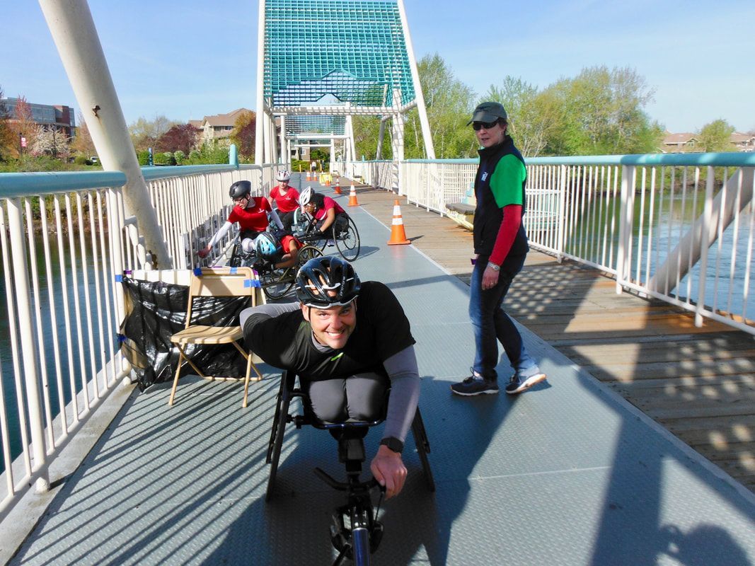 Racer in a black shirt grins on a footbridge as a volunteer in green walks by