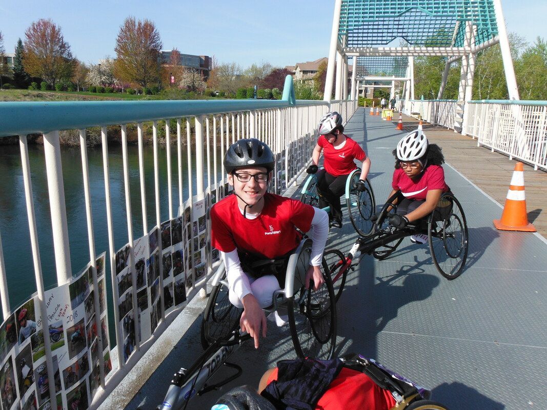 Racers in red shirts gather on a footbridge railing hung with photos