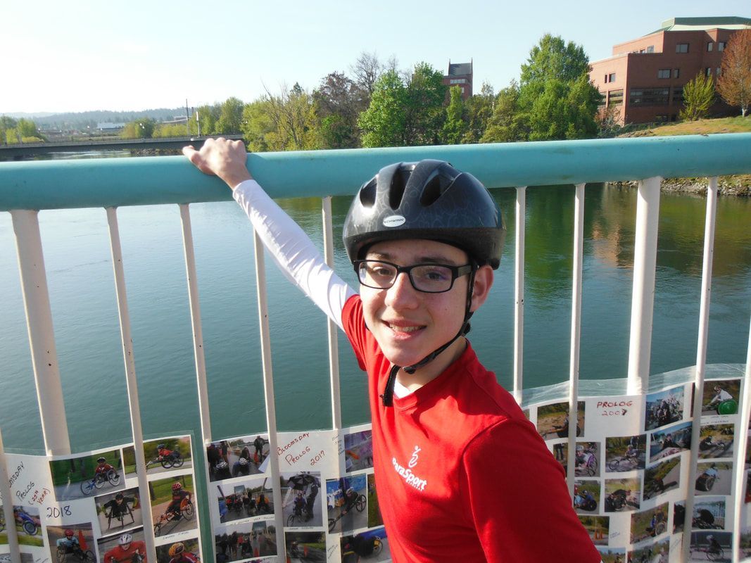 Smiling young athlete in a red ParaSport shirt leans on a railing over a river