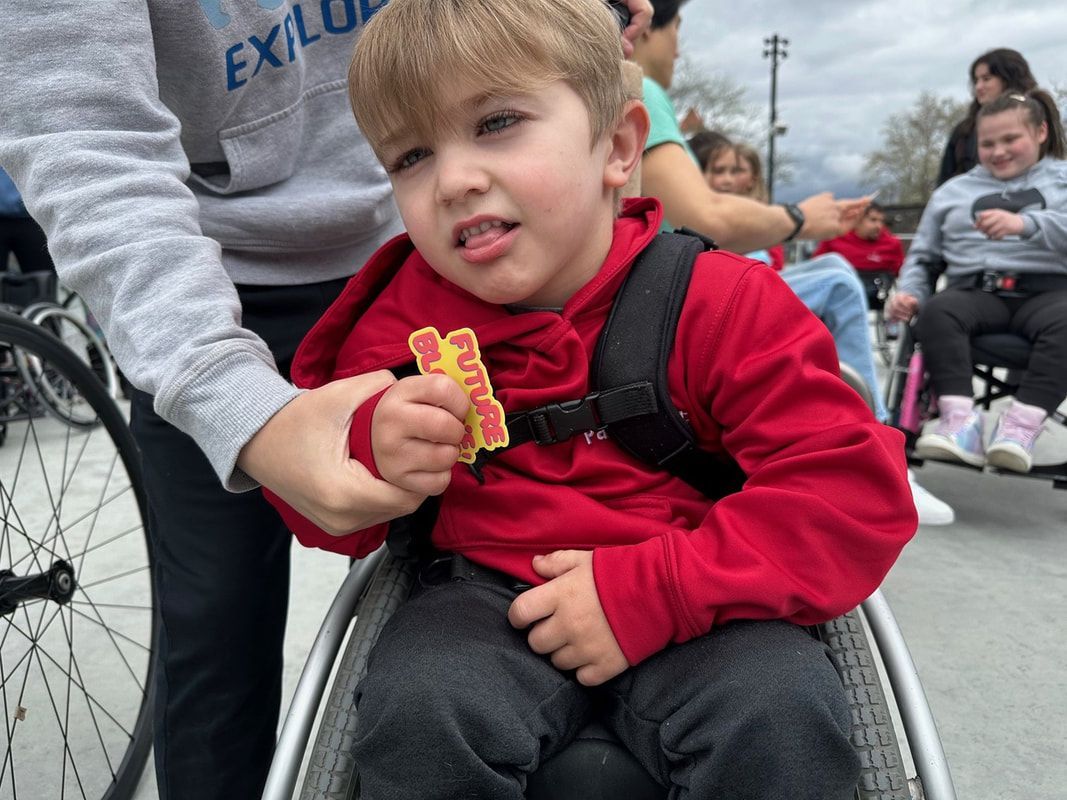 Boy in a red hoodie shows his Future Bloomie badge from his wheelchair
