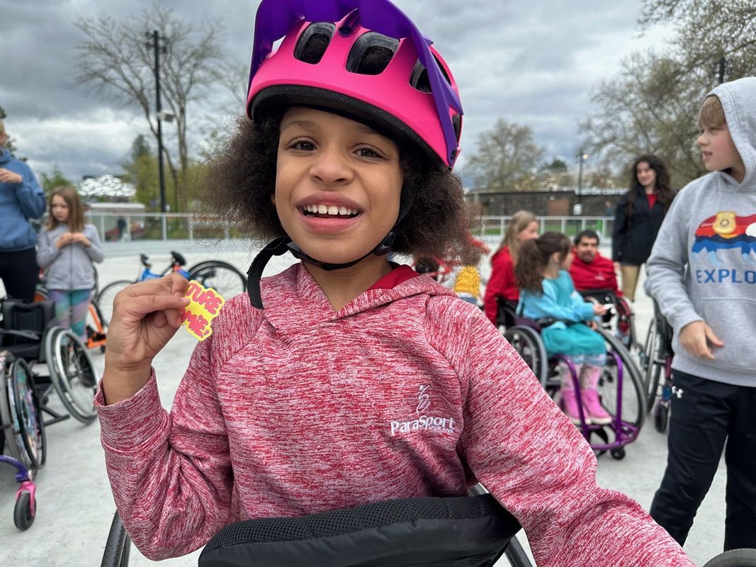 Smiling girl in a pink helmet holds up her Future Bloomie badge