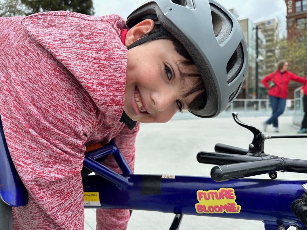 Smiling boy in a gray helmet leans over his blue adaptive bike