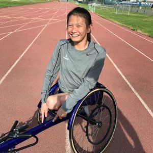 Hannah Dederick in a gray top sits in her racing wheelchair on a track
