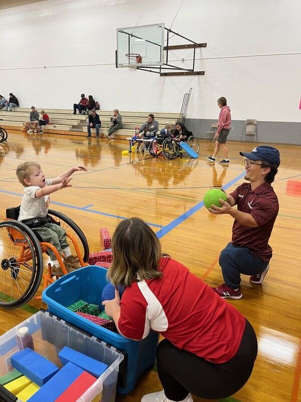Child in an orange wheelchair plays catch with a coach