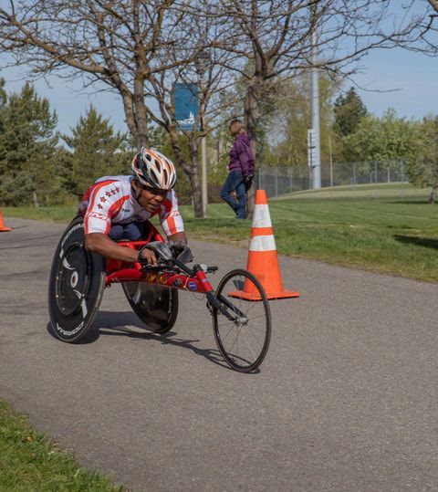Racer in a white and red jersey rounds an orange cone in a red racing chair