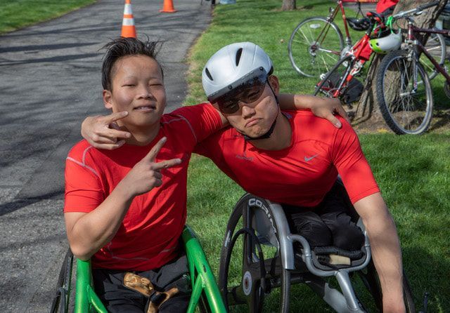 Two athletes in red shirts pose arm in arm, one flashing peace signs