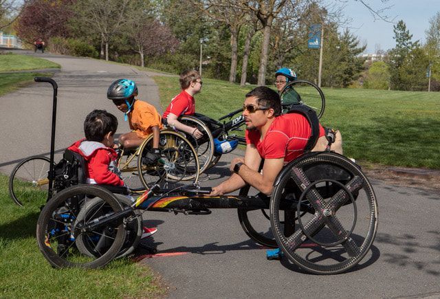 Adult racer in a red shirt chats with young racers beside a park path