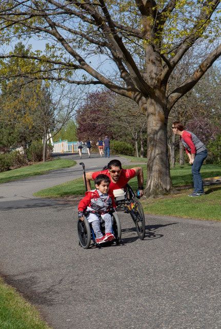 Man in a racing chair and a boy in a wheelchair roll down a tree-lined path