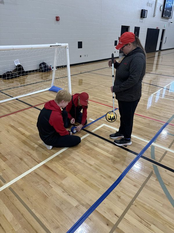 Two volunteers tape a blue goalball line as a third holds a measuring wheel