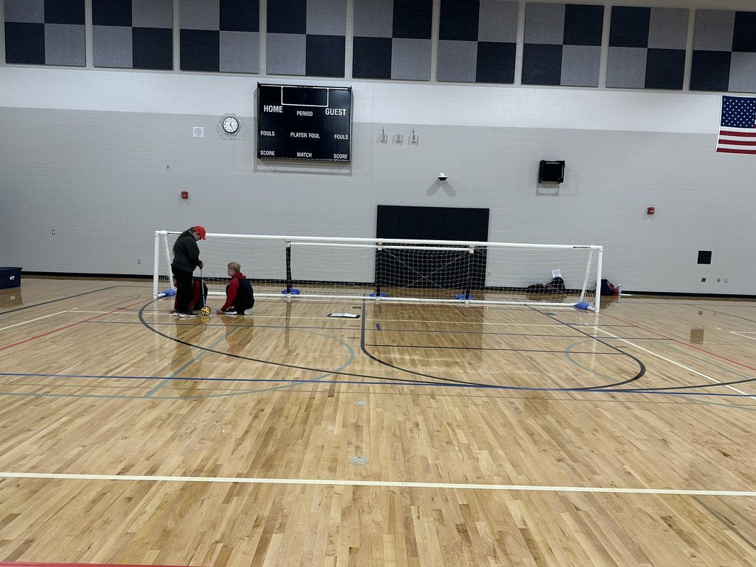 Volunteers tape goalball court lines in a gym in front of a white goal net
